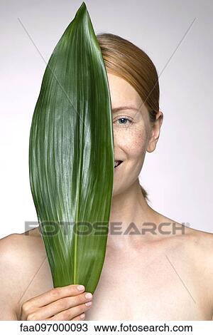 Young woman holding up leaf concealing part of face View Large Photo Image Stock Image - Young woman holding up leaf concealing part of face. Fotosearch
