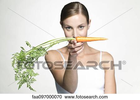 Young woman holding up raw carrot View Large Photo Image Stock Image - Young woman holding up raw carrot. Fotosearch