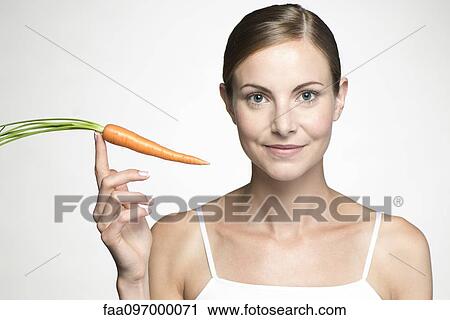 Young woman holding up raw carrot View Large Photo Image Stock Image - Young woman holding up raw carrot. Fotosearch