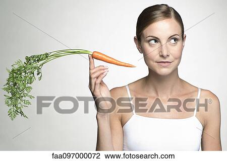 Young woman holding up raw carrot View Large Photo Image Stock Image - Young woman holding up raw carrot. Fotosearch