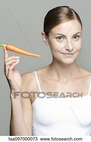 Stock Image - Young woman holding up raw carrot. Fotosearch
