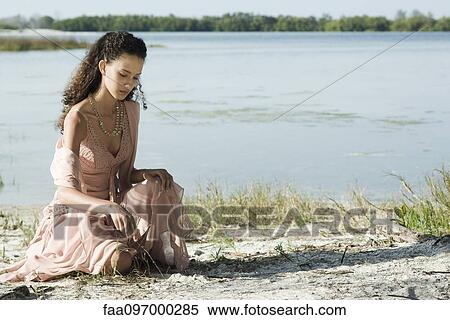 Young woman in dress sitting by lake, drawing in sand with stick View Large Photo Image Stock Photography - Young woman in dress sitting by lake, drawing in sand with stick. Fotosearch