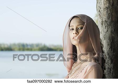 Young woman leaning against tree, wearing head scarf View Large Photo Image Stock Image - Young woman leaning against tree, wearing head scarf. Fotosearch