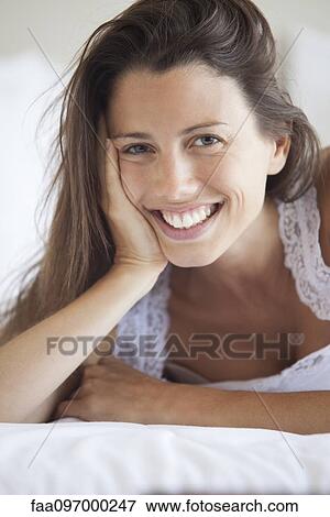Stock Photo - Young woman lying on stomach, leaning on elbow, portrait. Fotosearch