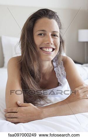 Stock Photo - Young woman lying on stomach, leaning on elbow, portrait. Fotosearch