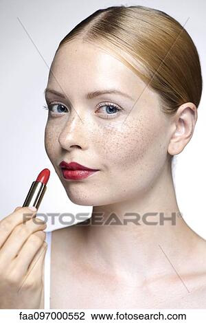 Stock Image - Young woman putting on lipstick. Fotosearch