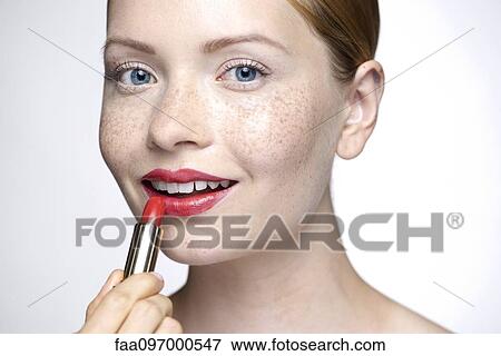 Stock Photo - Young woman putting on lipstick. Fotosearch