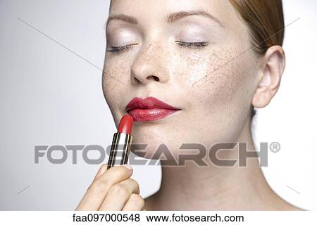 Stock Photo - Young woman putting on lipstick. Fotosearch