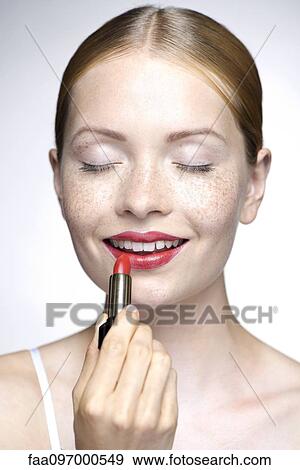 Stock Photo - Young woman putting on lipstick. Fotosearch
