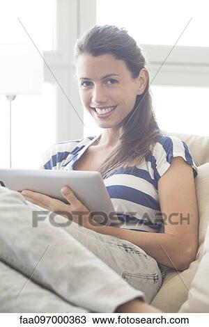 Stock Image - Young woman relaxing at home using digital tablet. Fotosearch