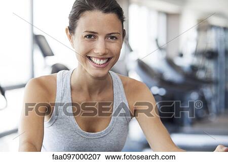 Stock Photo - Young woman using exercise machine at gym. Fotosearch