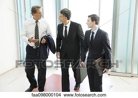 Picture - Business associates chatting while entering office building together. Fotosearch