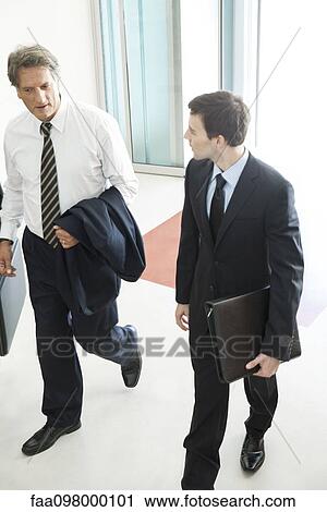 Stock Image - Business associates chatting while entering office building together. Fotosearch