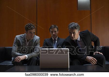 Stock Photo - Business associates sitting side by side on sofa looking at laptop computer in disbelief. Fotosearch