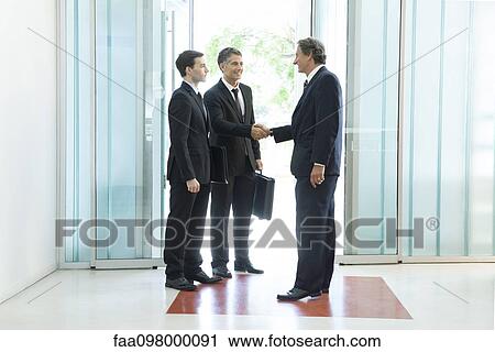Stock Image - Businessman meeting associates in office lobby. Fotosearch