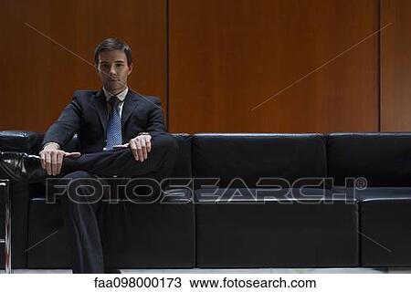 Stock Image - Businessman sitting in waiting room, portrait. Fotosearch