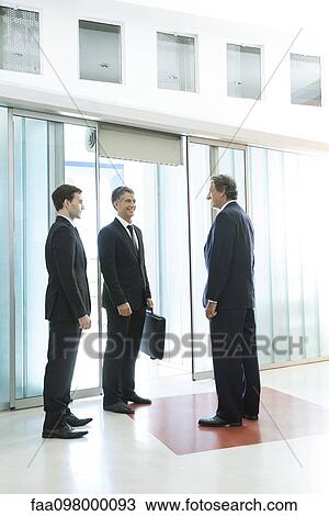 Stock Image - Businessmen chatting in building lobby. Fotosearch