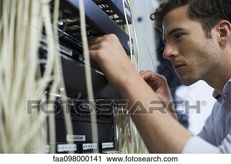 Stock Image - Computer technician performing maintenance on computer networking equipment. Fotosearch