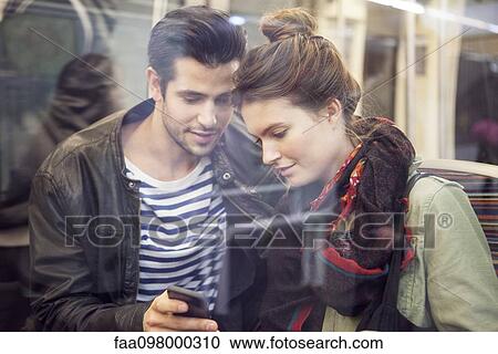 Couple on subway looking at smartphone together View Large Photo Image Stock Image - Couple on subway looking at smartphone together. Fotosearch