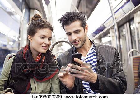 Friends riding subway looking at smartphone together View Large Photo Image Stock Photo - Friends riding subway looking at smartphone together. Fotosearch