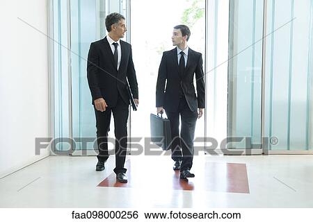 Senior business executive chatting with new associate as they enter building together View Large Photo Image Stock Photograph - Senior business executive chatting with new associate as they enter building together. Fotosearch