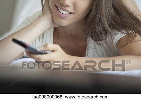 Stock Photo - Woman lying down watching TV, cropped. Fotosearch
