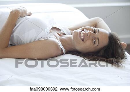 Woman lying on bed, smiling, portrait View Large Photo Image Stock Image - Woman lying on bed, smiling, portrait. Fotosearch