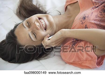 Stock Photo - Woman lying on bed, talking on cell phone. Fotosearch