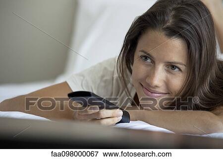 Stock Photo - Woman lying on bed watching TV. Fotosearch