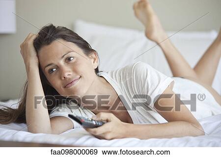Stock Photo - Woman lying on bed watching TV. Fotosearch