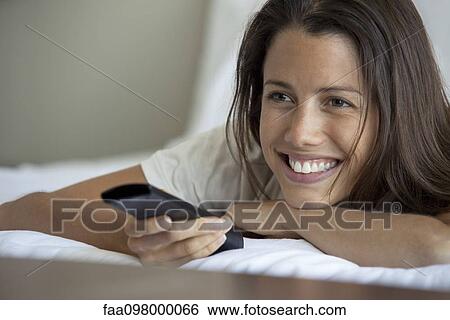Stock Photograph - Woman lying on bed watching TV. Fotosearch