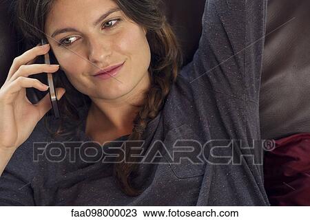 Stock Image - Woman reclining on sofa talking on cell phone. Fotosearch