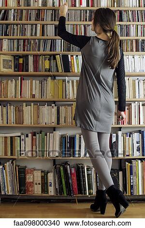 Stock Image - Woman selecting book from shelf, rear view. Fotosearch