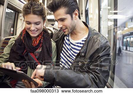 Young couple riding subway looking at digital tablet together View Large Photo Image Stock Image - Young couple riding subway looking at digital tablet together. Fotosearch