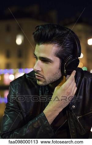 Young man outdoors at night listening to music with headphones View Large Photo Image Stock Image - Young man outdoors at night listening to music with headphones. Fotosearch