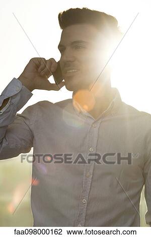 Stock Image - Young man talking on cell phone, silhouette. Fotosearch