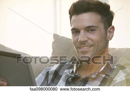 Stock Image - Young man using digital tablet at home. Fotosearch