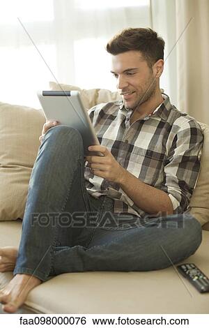 Young man using digital tablet at home View Large Photo Image Stock Photograph - Young man using digital tablet at home. Fotosearch
