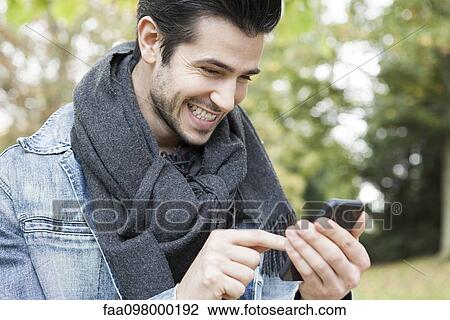 Stock Image - Young man using smartphone outdoors. Fotosearch
