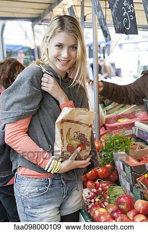 Stock Photo - Young woman at greengrocer's buying fresh fruits and vegetables. Fotosearch