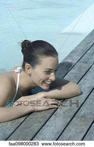 Stock Image - Young woman leaning on poolside, smiling. Fotosearch