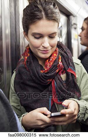 Stock Photography - Young woman on subway using smartphone. Fotosearch