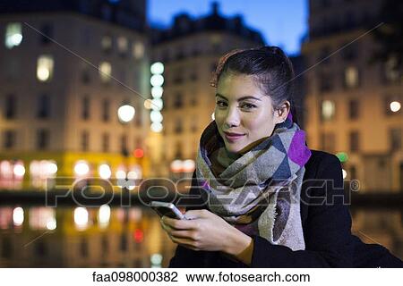 Stock Image - Young woman outdoors using smartphone, portrait. Fotosearch