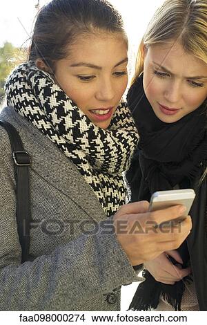 Picture - Young women outdoors looking at cell phone together. Fotosearch