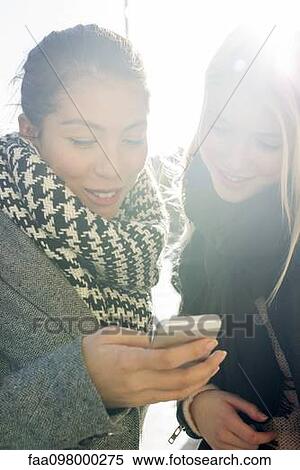 Young women outdoors looking at cell phone together View Large Photo Image Stock Photography - Young women outdoors looking at cell phone together. Fotosearch