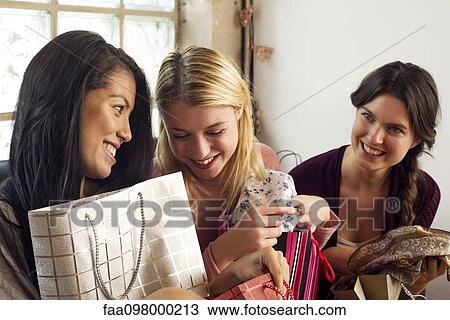 Stock Image - Young women showing off contents of shopping bags. Fotosearch