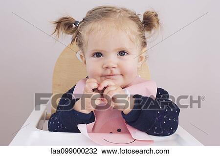 Stock Image - Baby girl sitting in high chair, portrait. Fotosearch