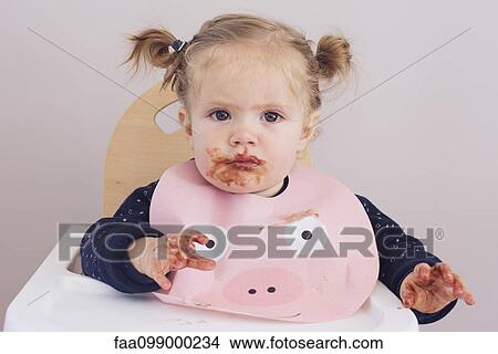 Baby girl sitting in high chair with food smeared on her face and hands View Large Photo Image Picture - Baby girl sitting in high chair with food smeared on her face and hands. Fotosearch
