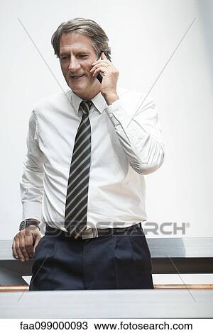 Stock Image - Businessman leaning against railing, talking on cell phone. Fotosearch