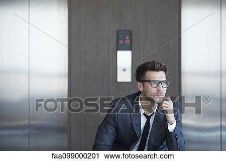 Stock Image - Businessman sitting in lobby, looking away in thought. Fotosearch
